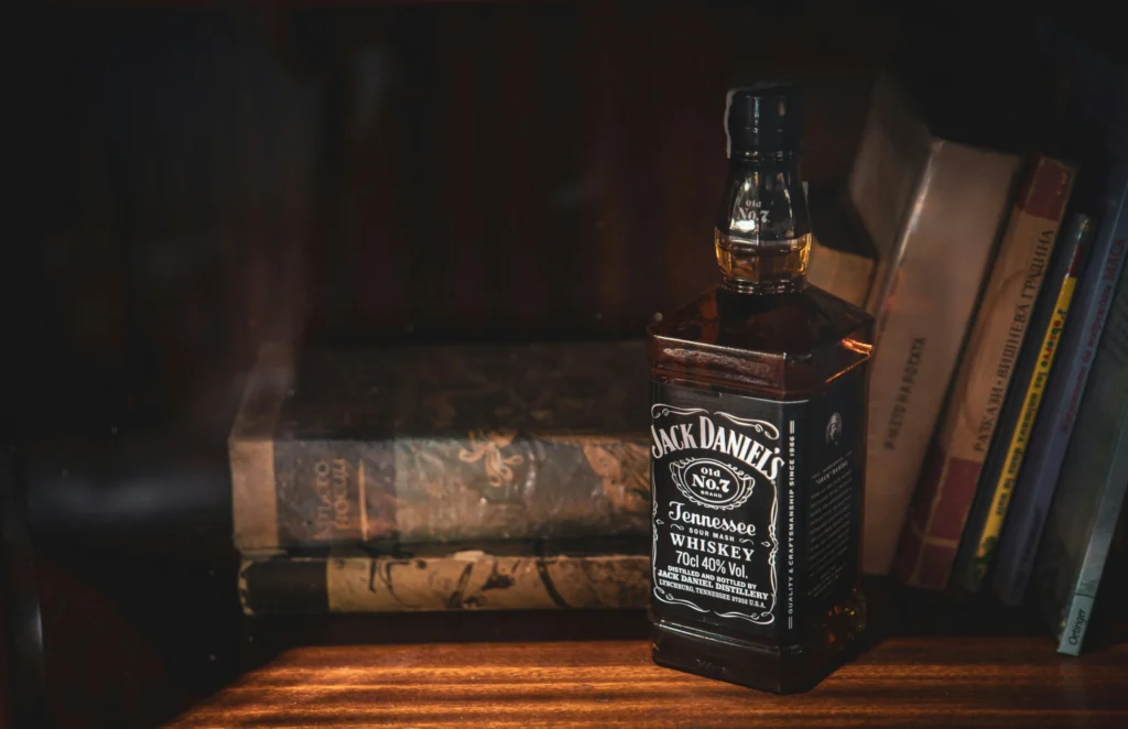 Whiskey atau Whisky? Panduan Ringkas Buat Pecinta Spirit 6 Botol whiskey Jack Daniel's di samping buku